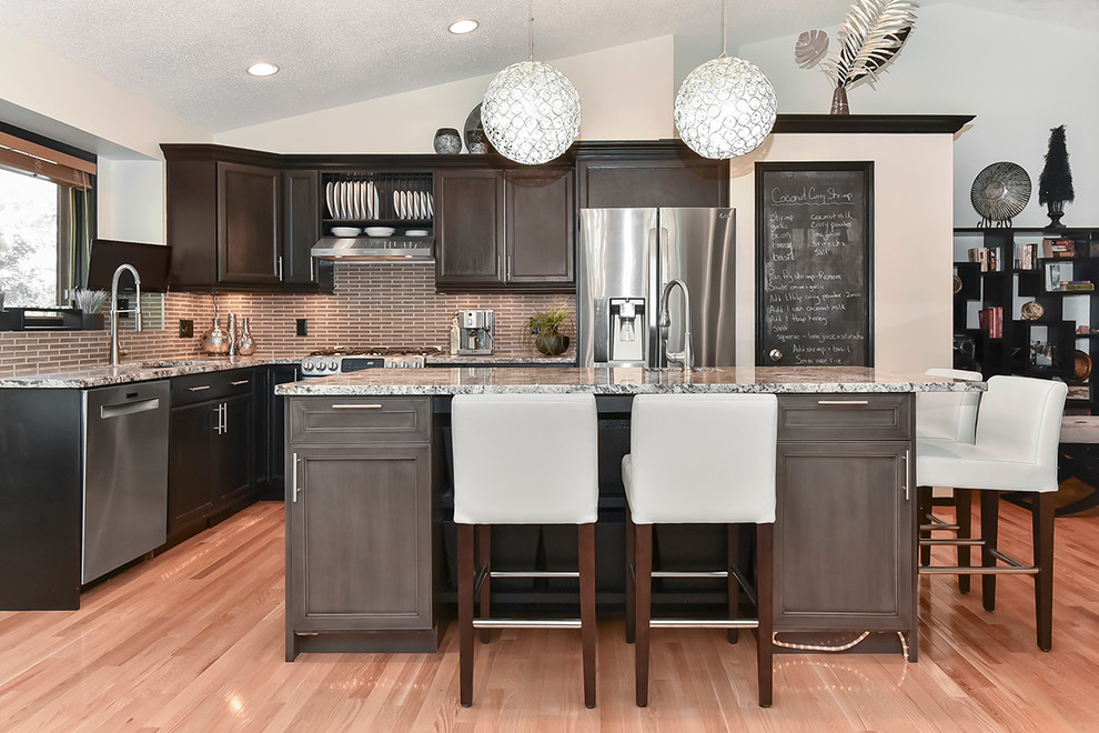 Design ideas for a large transitional open plan kitchen in Calgary with an undermount sink, recessed-panel cabinets, black cabinets, granite benchtops, brown splashback, glass tile splashback, stainless steel appliances, medium hardwood floors and with island.