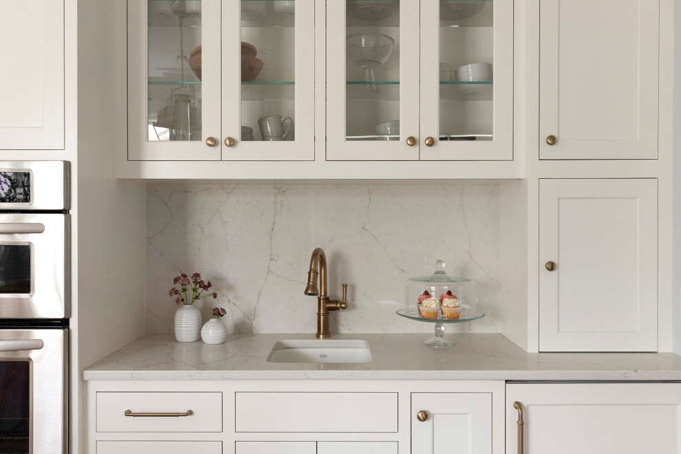 Inspiration for a large transitional l-shaped eat-in kitchen in Minneapolis with a farmhouse sink, glass-front cabinets, white cabinets, quartzite benchtops, white splashback, engineered quartz splashback, panelled appliances, light hardwood floors, with island, brown floor and white benchtop.