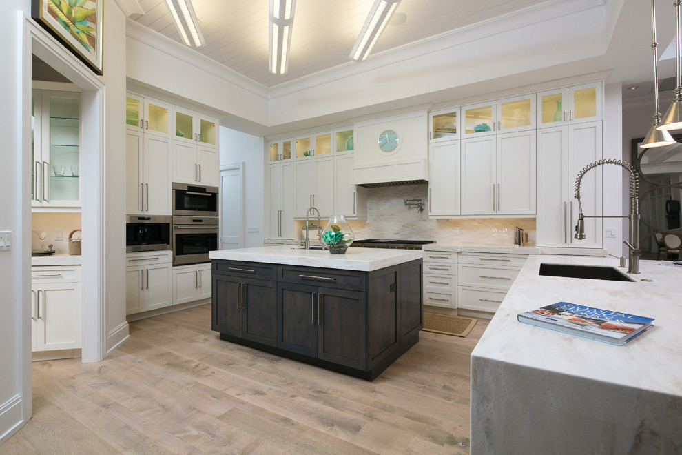 Eat-in kitchen - large transitional u-shaped light wood floor eat-in kitchen idea in Miami with an undermount sink, shaker cabinets, white cabinets, marble countertops, white backsplash, stone slab backsplash, stainless steel appliances and an island