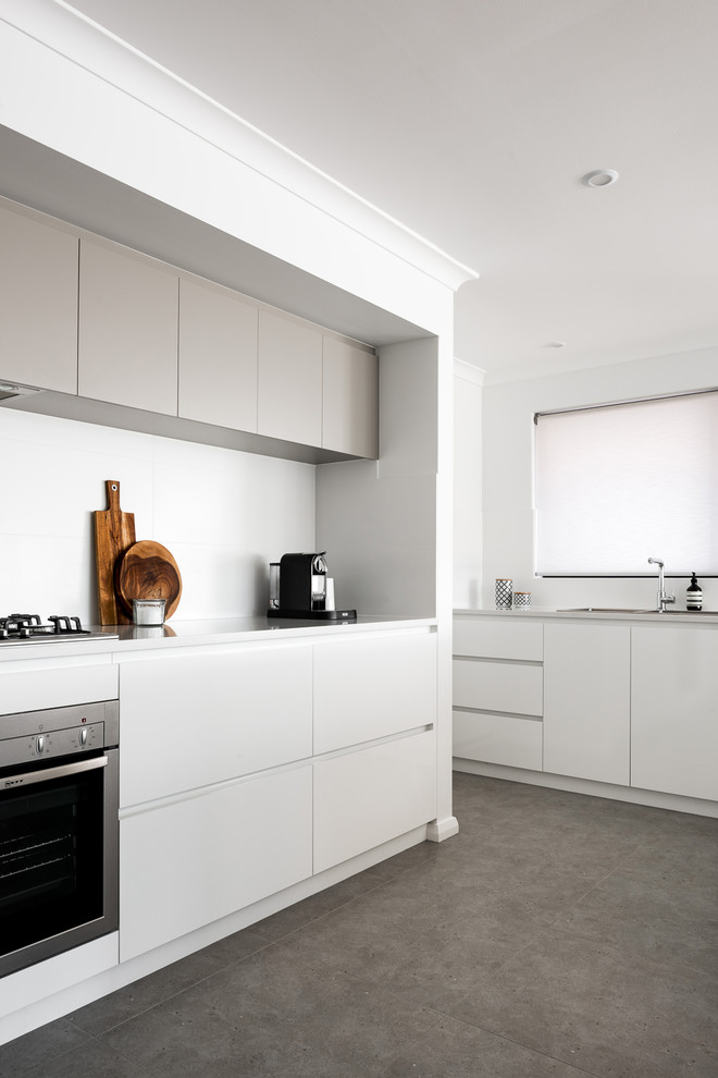 Photo of a large modern galley open plan kitchen in Perth with a drop-in sink, flat-panel cabinets, white cabinets, quartz benchtops, white splashback, porcelain splashback, stainless steel appliances, porcelain floors, with island and brown floor.