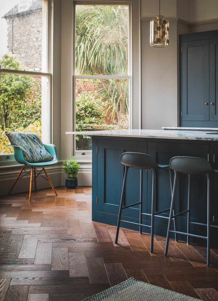 This is an example of a large contemporary l-shaped eat-in kitchen in Other with a farmhouse sink, shaker cabinets, blue cabinets, marble benchtops, blue splashback, cement tile splashback, stainless steel appliances, dark hardwood floors, with island and brown floor.