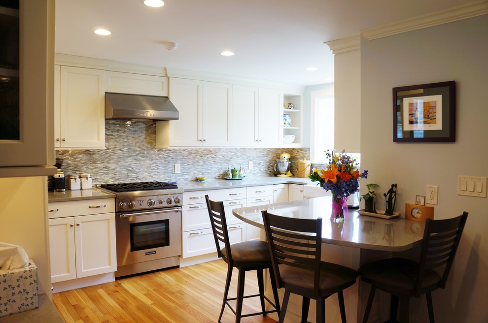 Inspiration for a mid-sized transitional l-shaped light wood floor eat-in kitchen remodel in Boston with a farmhouse sink, shaker cabinets, white cabinets, quartz countertops, blue backsplash, glass tile backsplash, paneled appliances and a peninsula
