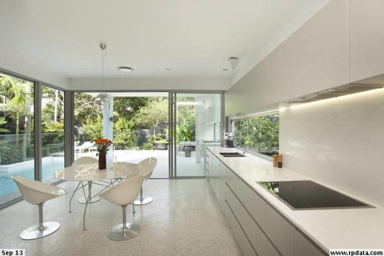 Small contemporary single-wall kitchen in Brisbane with an undermount sink, quartz benchtops, white splashback, stone slab splashback, black appliances, concrete floors and no island.
