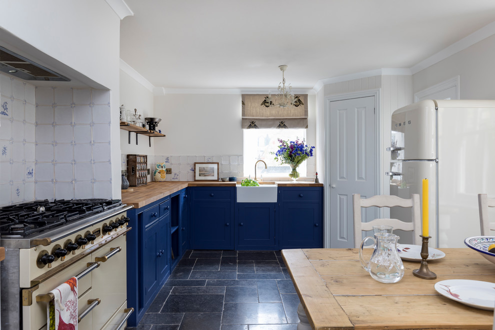 Photo of a large farmhouse l-shaped kitchen/diner in London with a belfast sink, shaker cabinets, blue cabinets, wood worktops, white splashback, ceramic splashback, integrated appliances, limestone flooring, no island and blue floors.
