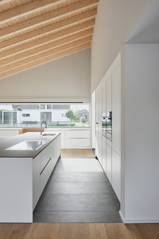 Modern single-wall eat-in kitchen in Cologne with a drop-in sink, flat-panel cabinets, white cabinets, granite benchtops, white splashback, timber splashback, stainless steel appliances, terrazzo floors, with island, grey floor, grey benchtop and exposed beam.
