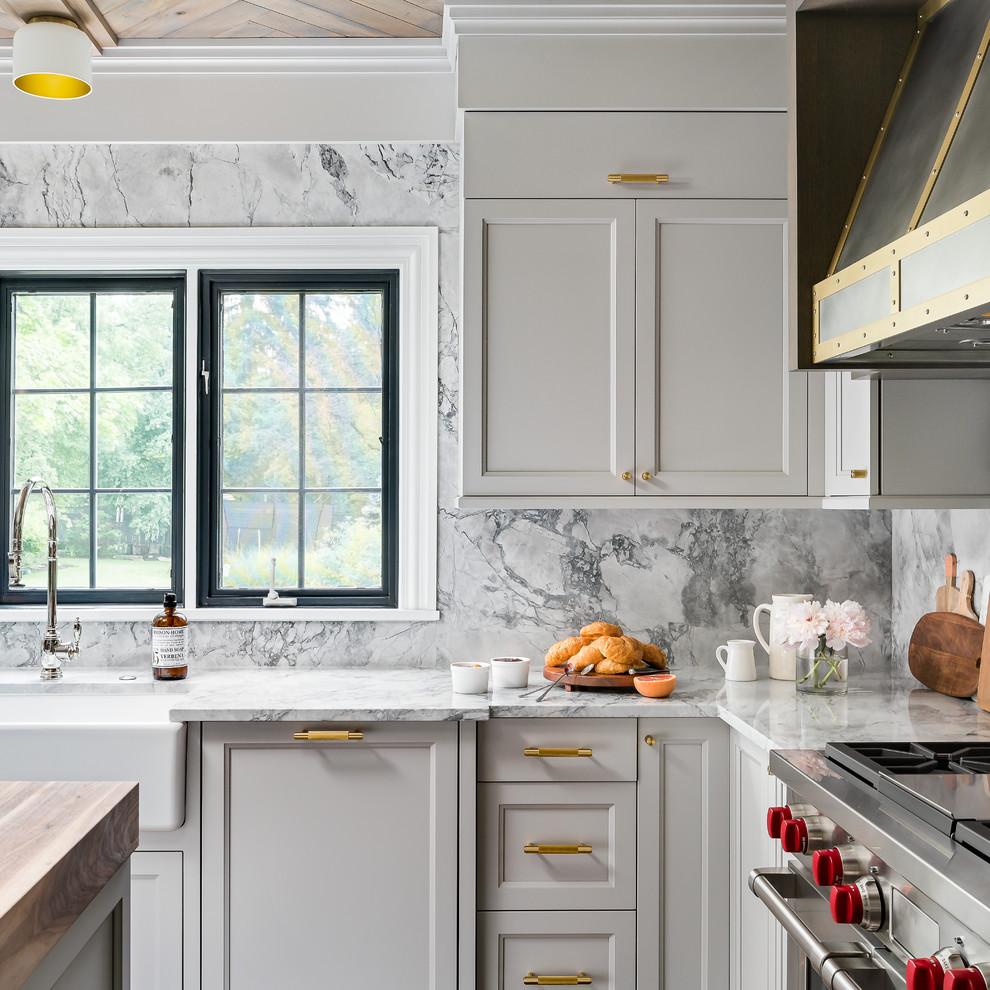 Example of a mid-sized transitional medium tone wood floor and brown floor enclosed kitchen design in Chicago with a farmhouse sink, recessed-panel cabinets, gray cabinets, quartzite countertops, gray backsplash, stone slab backsplash, paneled appliances, an island and gray countertops
