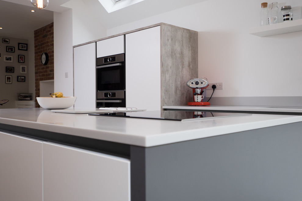 This is an example of a large contemporary single-wall open plan kitchen in Hampshire with an undermount sink, flat-panel cabinets, white cabinets, white splashback, stainless steel appliances and with island.
