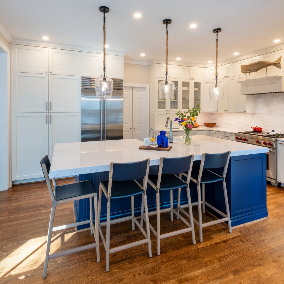 Photo of a mid-sized transitional l-shaped open plan kitchen in Richmond with a farmhouse sink, shaker cabinets, white cabinets, quartz benchtops, white splashback, ceramic splashback, stainless steel appliances, medium hardwood floors, with island, brown floor and white benchtop.