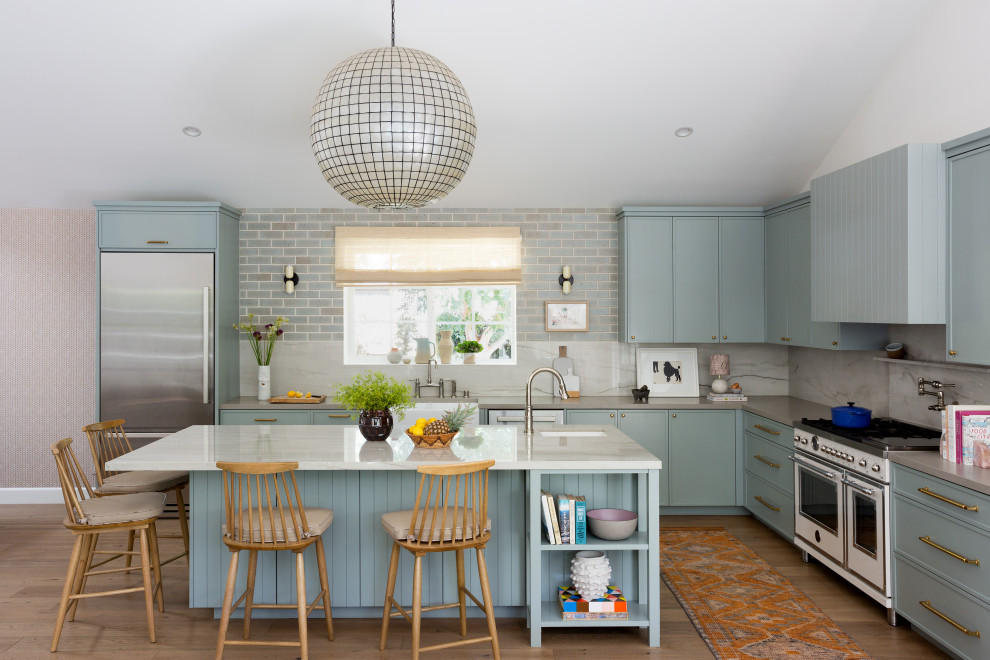 Inredning av ett klassiskt grå grått l-kök, med en rustik diskho, släta luckor, blå skåp, grått stänkskydd, stänkskydd i sten, vita vitvaror, mellanmörkt trägolv, en köksö och brunt golv