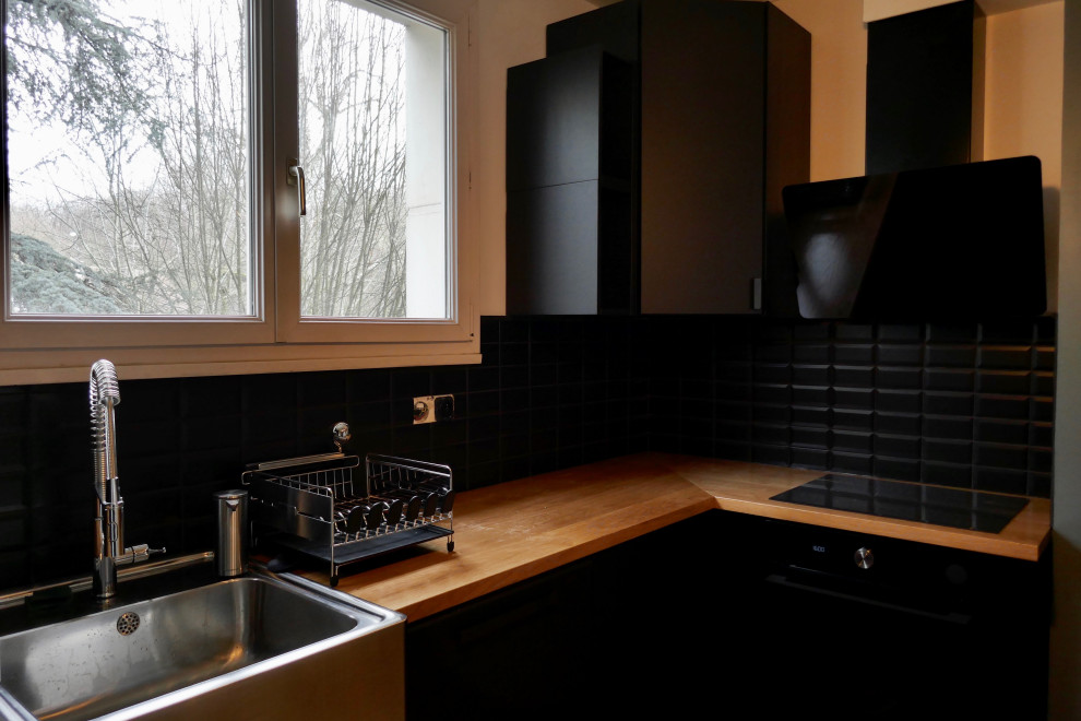 Photo of a mid-sized modern u-shaped separate kitchen in Paris with a drop-in sink, flat-panel cabinets, black cabinets, wood benchtops, black splashback, subway tile splashback, stainless steel appliances, vinyl floors, brown floor and brown benchtop.