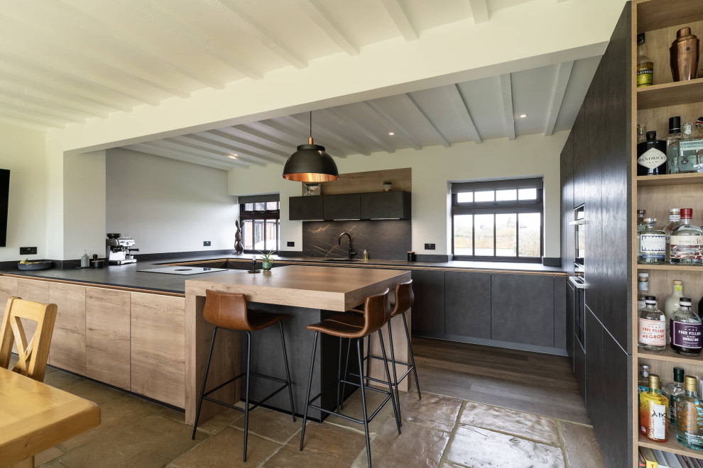 Photo of a large modern l-shaped open plan kitchen in Oxfordshire with flat-panel cabinets, black cabinets, quartz worktops, brown splashback, black appliances, a breakfast bar and black worktops.