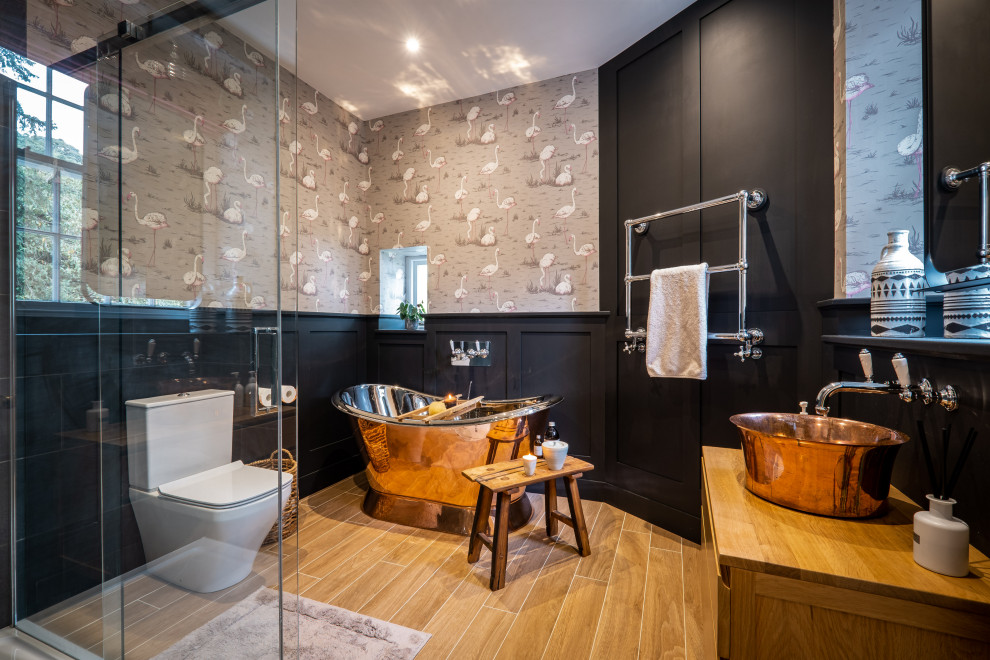 This is an example of a traditional bathroom in Other with flat-panel cabinets, medium wood cabinets, a freestanding bath, a corner shower, grey walls, wood-effect flooring, a vessel sink, wooden worktops, brown floors, a sliding door, brown worktops, a single sink, wainscoting and wallpapered walls.