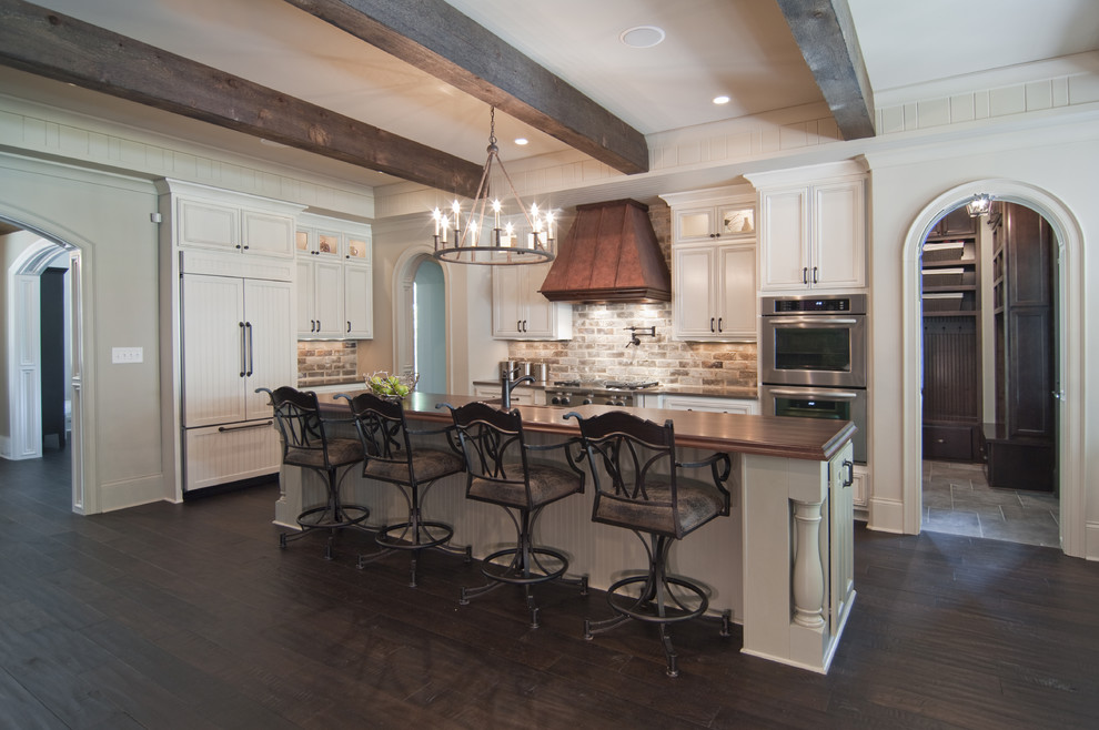 Design ideas for a large traditional galley eat-in kitchen in Charlotte with recessed-panel cabinets, white cabinets, wood benchtops, beige splashback, brick splashback, panelled appliances, dark hardwood floors, with island and brown floor.