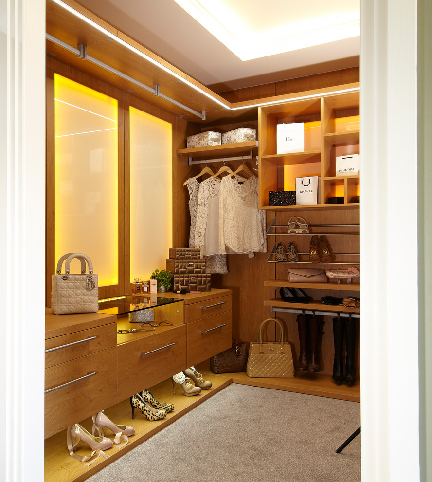 This is an example of a mid-sized contemporary gender-neutral walk-in wardrobe in London with medium wood cabinets and carpet.