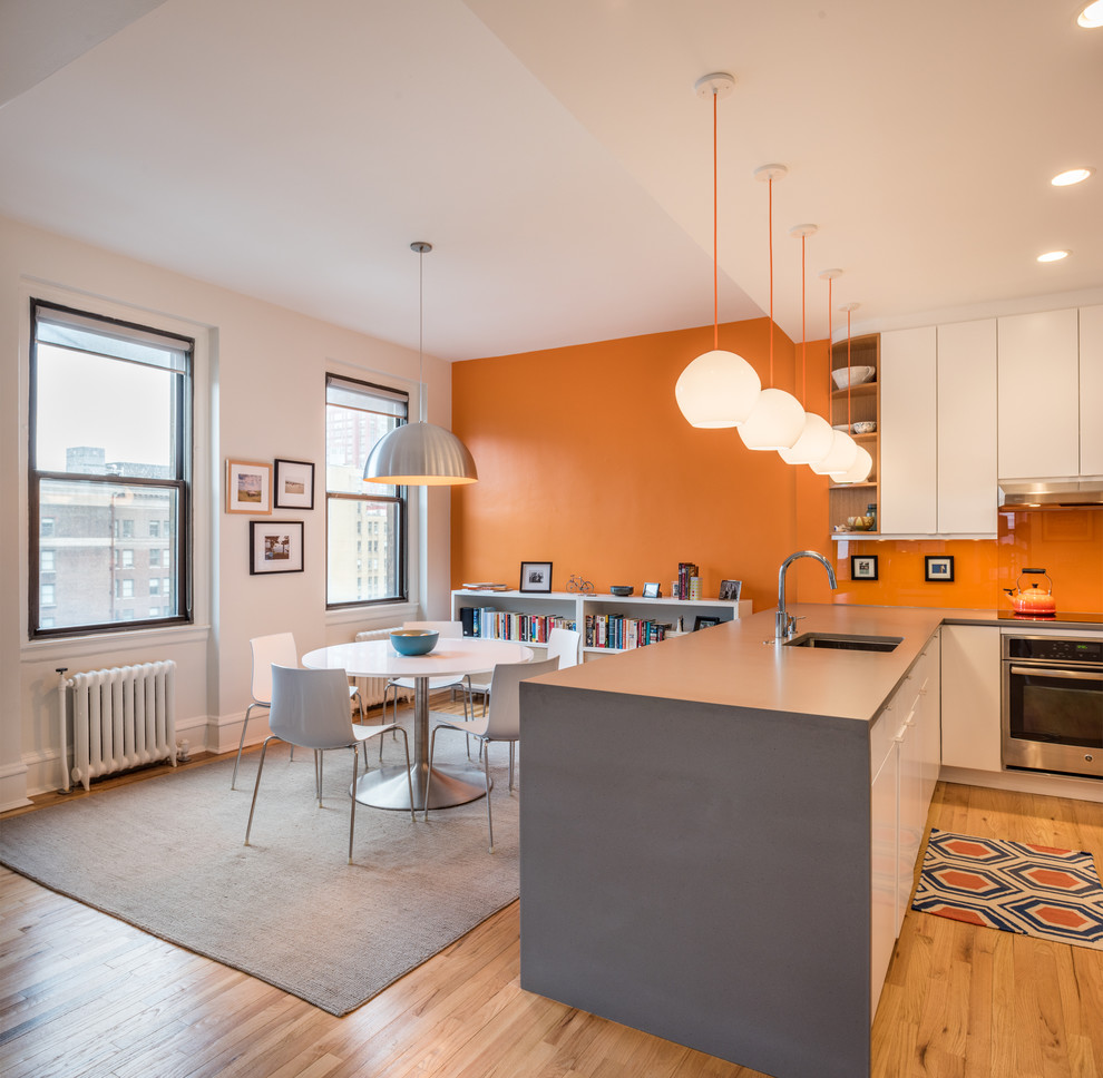 Inspiration for a contemporary u-shaped kitchen in Philadelphia with an undermount sink, flat-panel cabinets, white cabinets, orange splashback, stainless steel appliances, light hardwood floors and a peninsula.