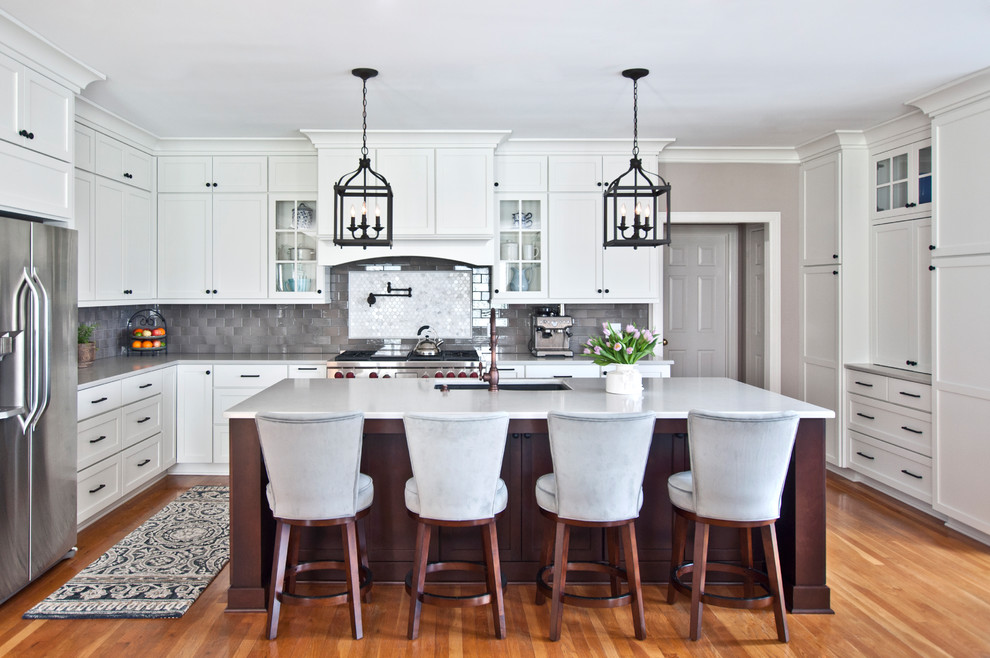 Inspiration for a traditional l-shaped kitchen in Nashville with an undermount sink, shaker cabinets, white cabinets, grey splashback, stainless steel appliances, medium hardwood floors, with island, brown floor and white benchtop.