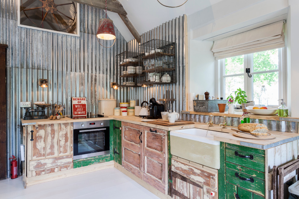 This is an example of an industrial l-shaped kitchen in London with a farmhouse sink, distressed cabinets, wood benchtops, metallic splashback and metal splashback.