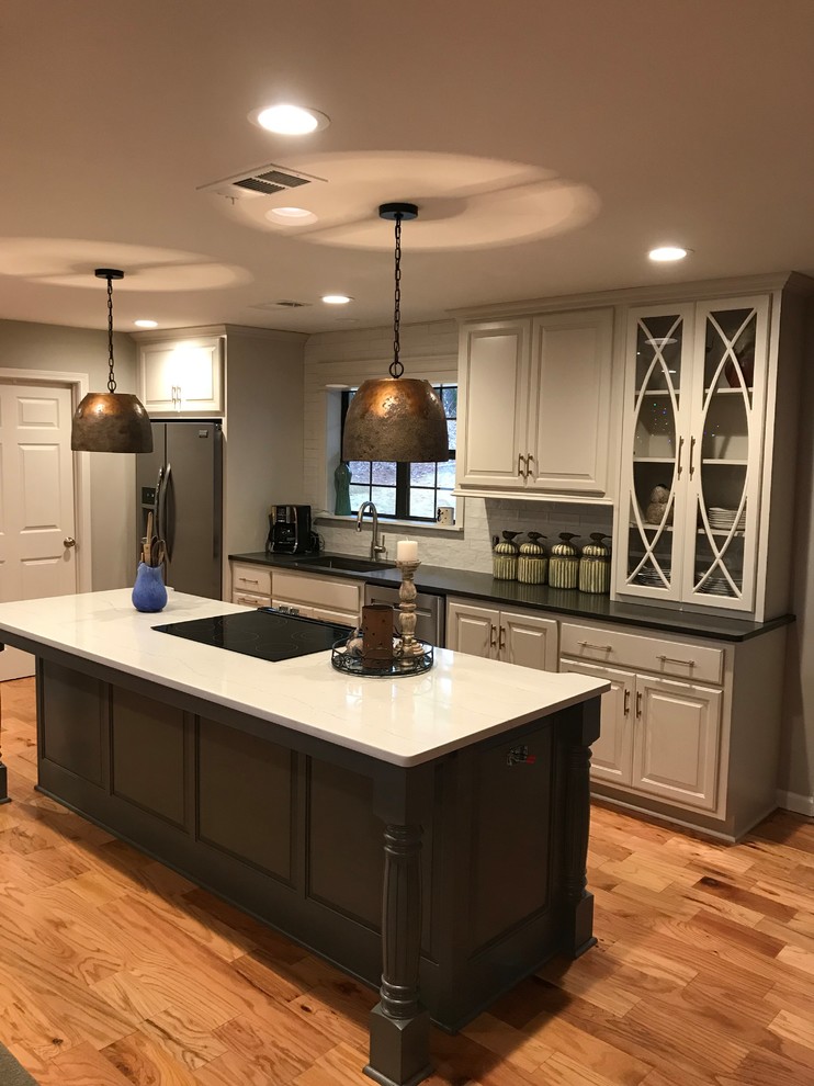 Example of a mid-sized transitional l-shaped medium tone wood floor and brown floor open concept kitchen design with an undermount sink, raised-panel cabinets, white cabinets, white backsplash, stainless steel appliances, an island and white countertops