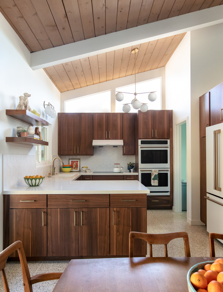Foto på ett stort retro kök, med en undermonterad diskho, släta luckor, skåp i mellenmörkt trä, bänkskiva i kvarts, vitt stänkskydd, stänkskydd i porslinskakel, vita vitvaror, terrazzogolv och beiget golv