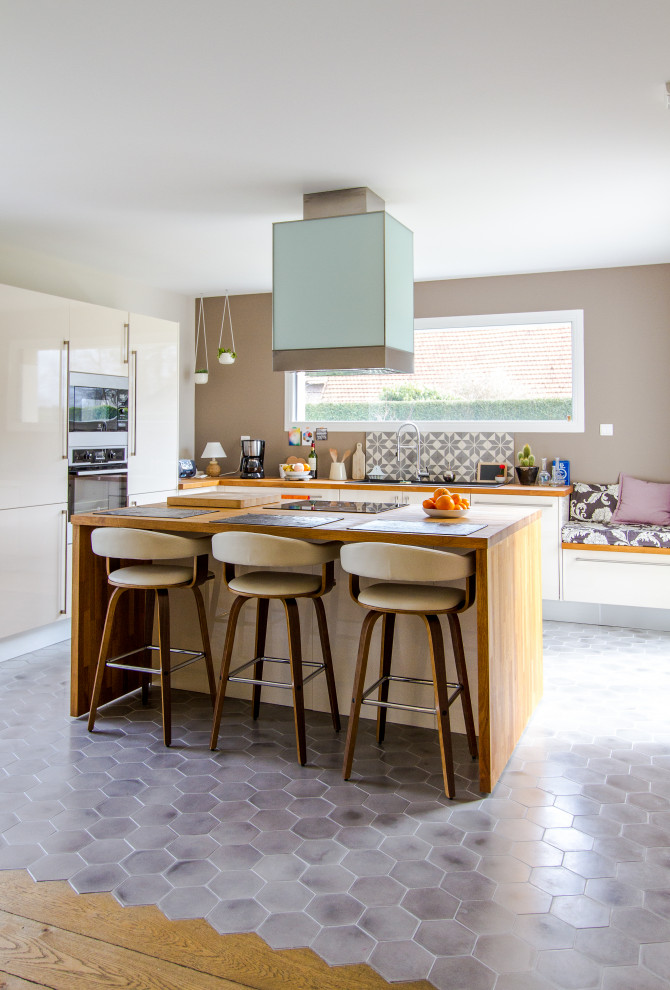 Inspiration for a contemporary l-shaped kitchen in Le Havre with flat-panel cabinets, beige cabinets, wood worktops, grey splashback, stainless steel appliances, an island, grey floors and brown worktops.
