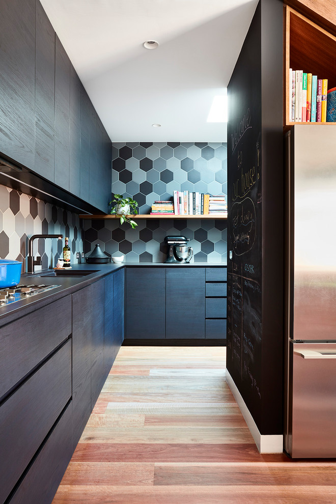Photo of a mid-sized contemporary l-shaped open plan kitchen in Melbourne with flat-panel cabinets, solid surface benchtops, black splashback, porcelain splashback, stainless steel appliances, medium hardwood floors, with island and brown floor.