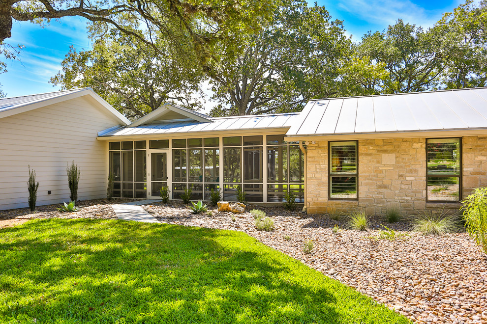 Photo of a large midcentury one-storey beige house exterior in Austin with mixed siding, a shed roof and a metal roof.