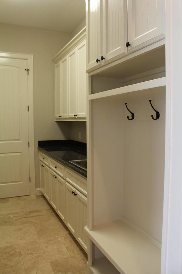 This is an example of a mid-sized traditional single-wall utility room in Houston with a drop-in sink, recessed-panel cabinets, white cabinets, granite benchtops, beige walls and travertine floors.