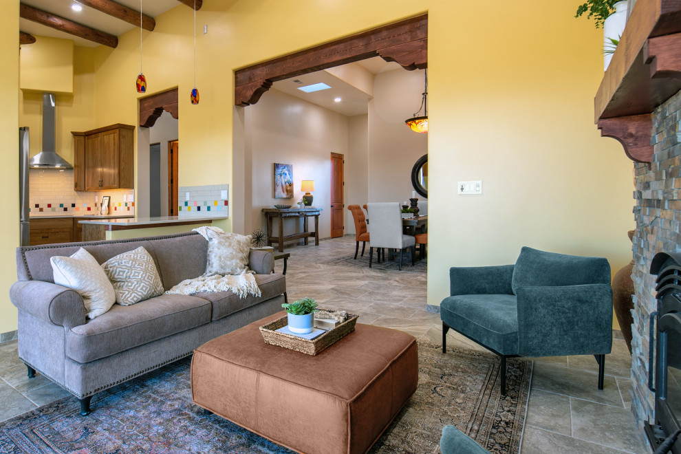 Пример оригинального дизайна: гостиная комната в стиле фьюжн с желтыми стенами, полом из травертина, стандартным камином, фасадом камина из каменной кладки, бежевым полом и балками на потолке