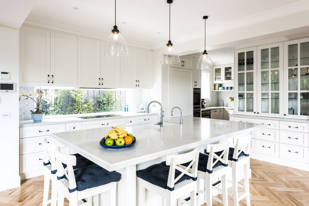 Large traditional l-shaped kitchen pantry with shaker cabinets, marble benchtops, grey splashback, mosaic tile splashback, medium hardwood floors, with island, an undermount sink, white cabinets and stainless steel appliances.