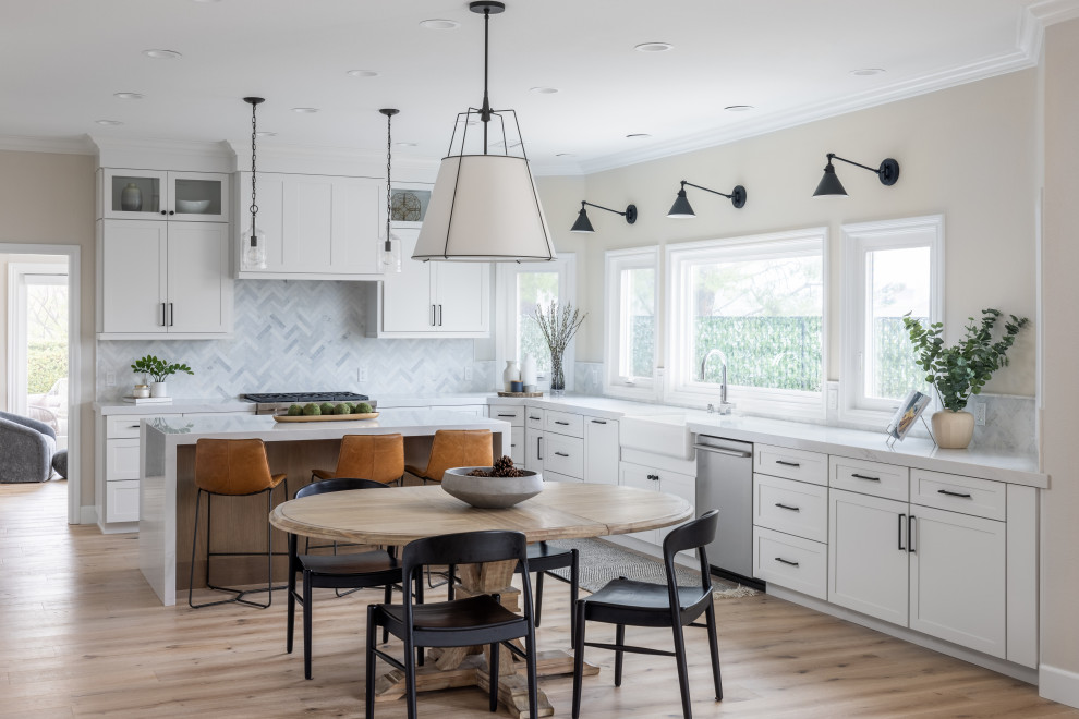 Eat-in kitchen - transitional l-shaped light wood floor and beige floor eat-in kitchen idea in Orange County with a farmhouse sink, shaker cabinets, white cabinets, gray backsplash, mosaic tile backsplash, stainless steel appliances, an island and white countertops