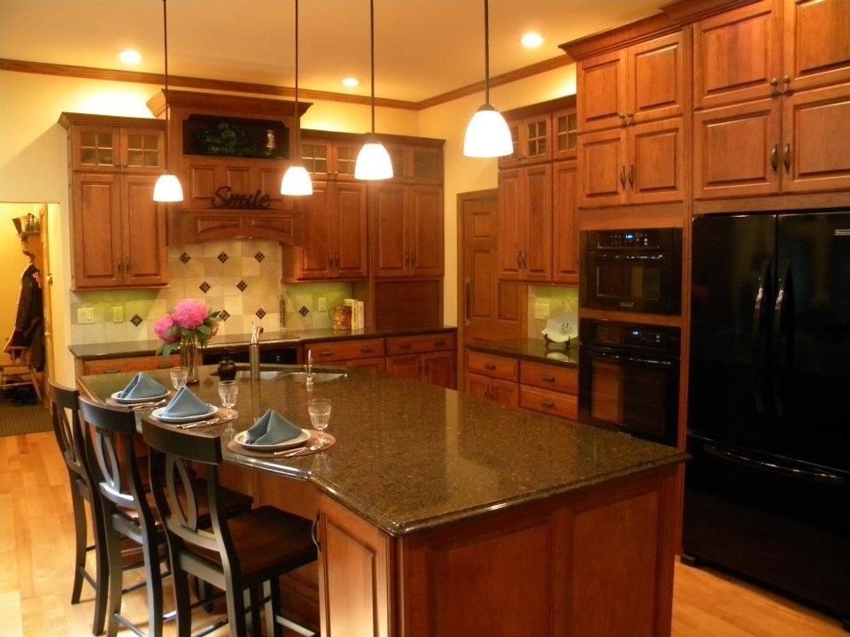 Mid-sized elegant l-shaped medium tone wood floor eat-in kitchen photo with a double-bowl sink, raised-panel cabinets, medium tone wood cabinets, granite countertops, beige backsplash, ceramic backsplash, black appliances and an island