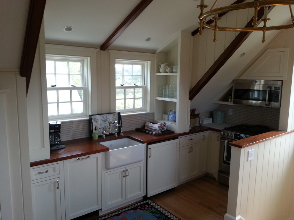 This is an example of a small traditional l-shaped open plan kitchen in Boston with an undermount sink, shaker cabinets, white cabinets, wood benchtops, beige splashback, matchstick tile splashback, stainless steel appliances, light hardwood floors, no island and brown floor.