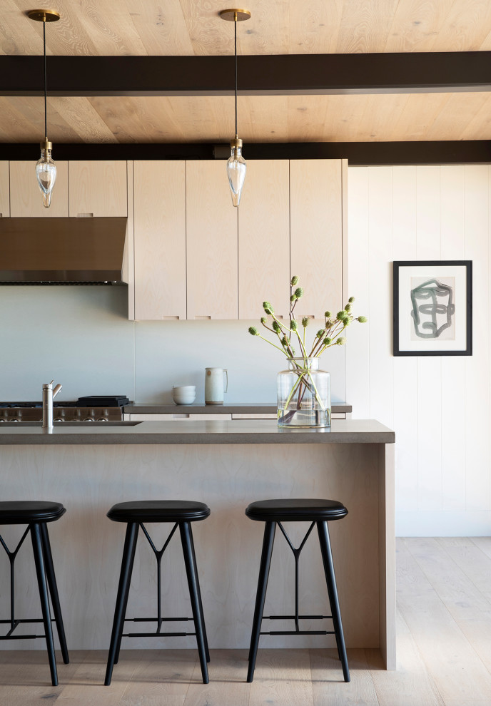 This is an example of a mid-sized modern open plan kitchen in San Francisco with flat-panel cabinets, light wood cabinets, concrete benchtops, white splashback, stainless steel appliances, light hardwood floors, with island and grey benchtop.