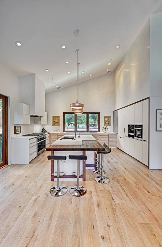 Expansive contemporary u-shaped eat-in kitchen in Sacramento with an undermount sink, flat-panel cabinets, white cabinets, quartz benchtops, white splashback, stainless steel appliances, light hardwood floors, with island, multi-coloured floor, white benchtop and vaulted.