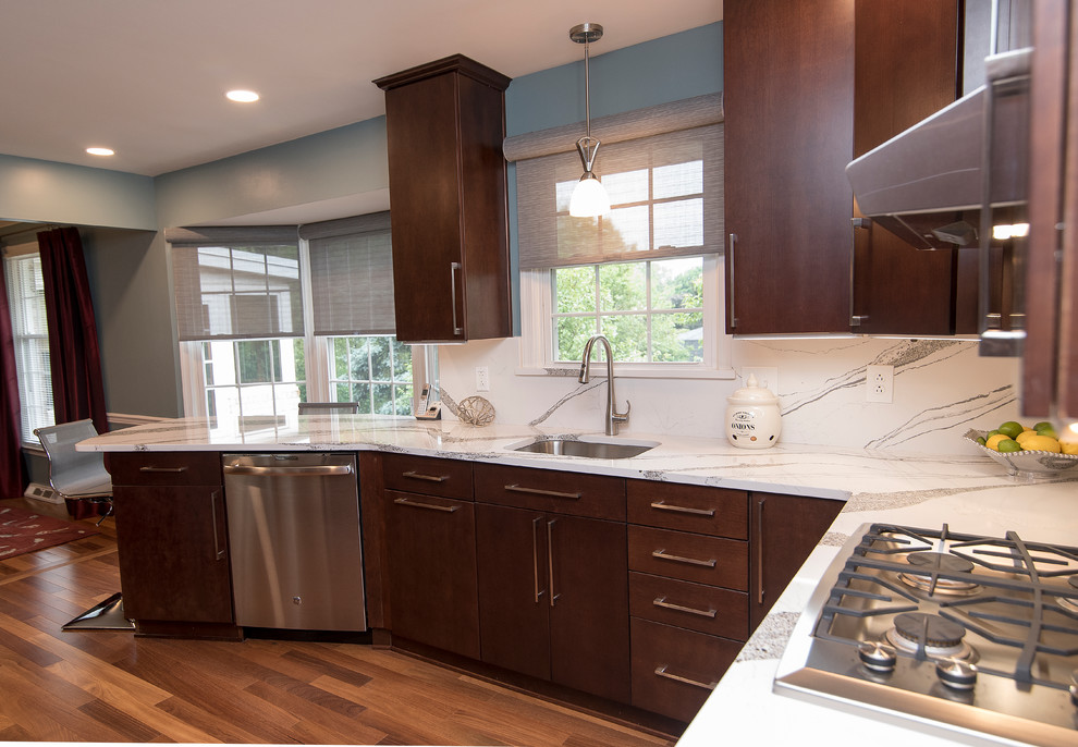 Mid-sized contemporary l-shaped kitchen pantry in Baltimore with a single-bowl sink, flat-panel cabinets, dark wood cabinets, quartz benchtops, white splashback, stainless steel appliances and white benchtop.