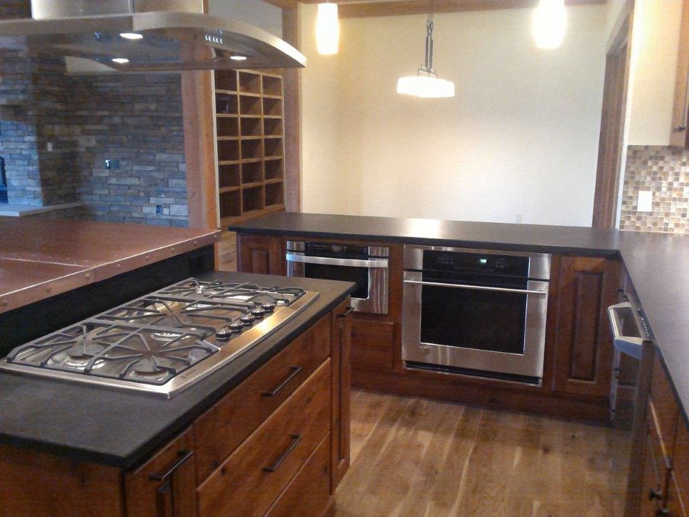 Large mountain style u-shaped medium tone wood floor and brown floor open concept kitchen photo with an undermount sink, raised-panel cabinets, dark wood cabinets, multicolored backsplash, glass tile backsplash, stainless steel appliances and an island