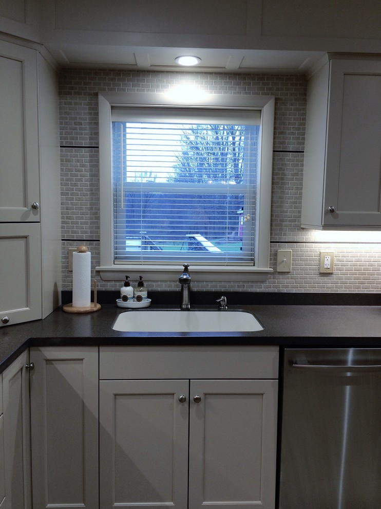Example of a mid-sized transitional u-shaped linoleum floor eat-in kitchen design with an integrated sink, recessed-panel cabinets, white cabinets, solid surface countertops, white backsplash, ceramic backsplash, stainless steel appliances and a peninsula