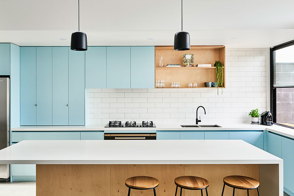 Design ideas for a beach style l-shaped eat-in kitchen in Geelong with an undermount sink, flat-panel cabinets, blue cabinets, white splashback, stainless steel appliances, with island, grey floor and white benchtop.