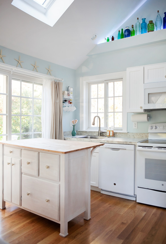 This is an example of a beach style kitchen in Boston with shaker cabinets, white cabinets, white appliances, medium hardwood floors and with island.