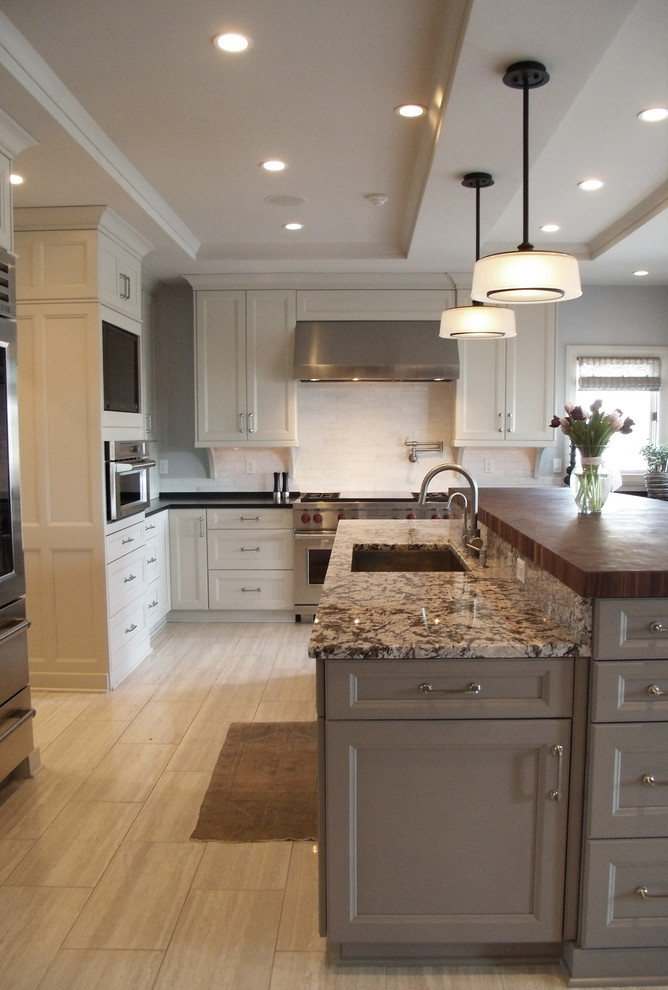 Mid-sized transitional l-shaped porcelain tile and beige floor enclosed kitchen photo with an undermount sink, recessed-panel cabinets, white cabinets, wood countertops, white backsplash, subway tile backsplash, stainless steel appliances and an island