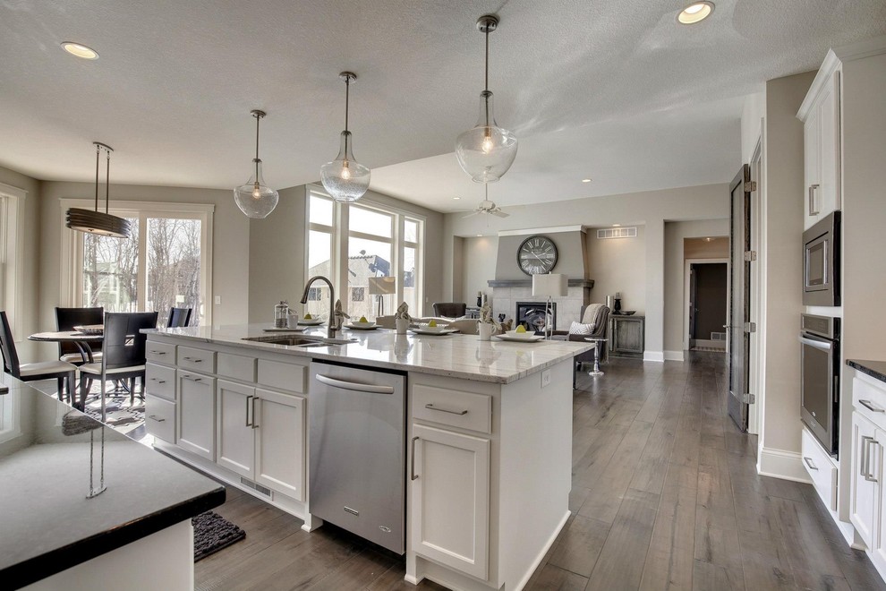 This is an example of a mid-sized transitional l-shaped open plan kitchen in Minneapolis with a double-bowl sink, shaker cabinets, white cabinets, granite benchtops, grey splashback, subway tile splashback, stainless steel appliances, dark hardwood floors and with island.