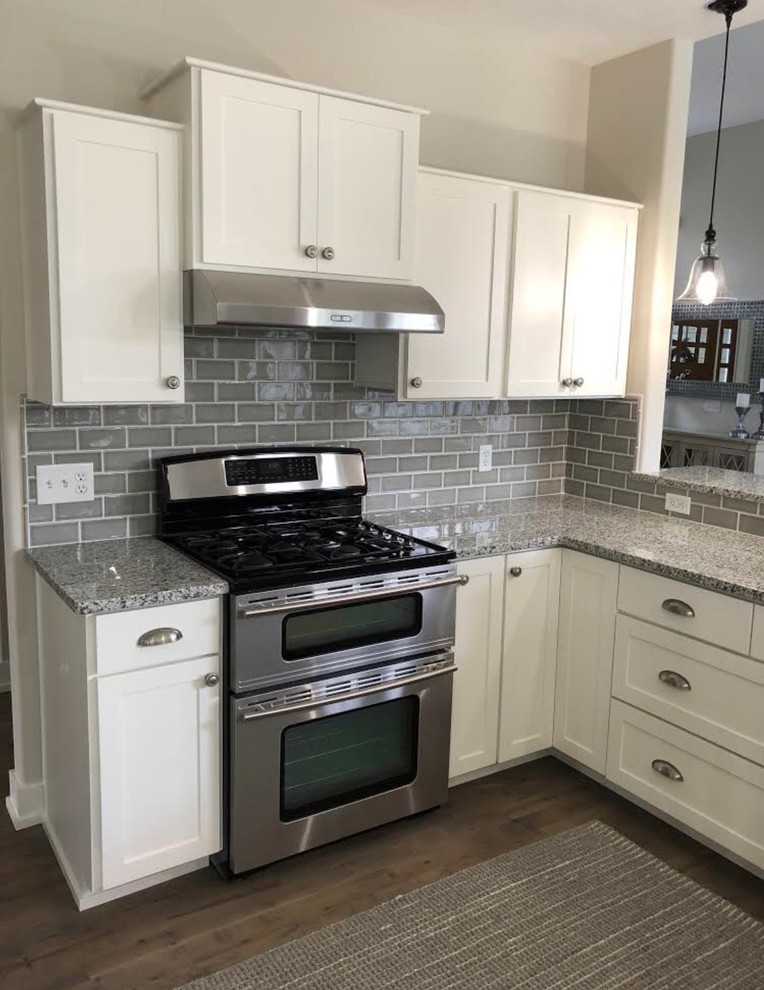 Mid-sized contemporary open plan kitchen in Grand Rapids with shaker cabinets, white cabinets, granite benchtops, grey splashback, subway tile splashback, stainless steel appliances, dark hardwood floors, a peninsula and brown floor.