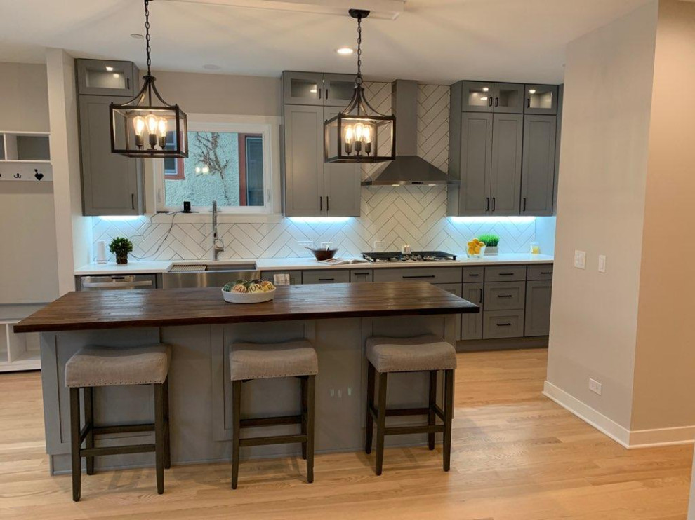 Eat-in kitchen - mid-sized transitional medium tone wood floor eat-in kitchen idea in Chicago with a farmhouse sink, shaker cabinets, gray cabinets, subway tile backsplash, stainless steel appliances and an island