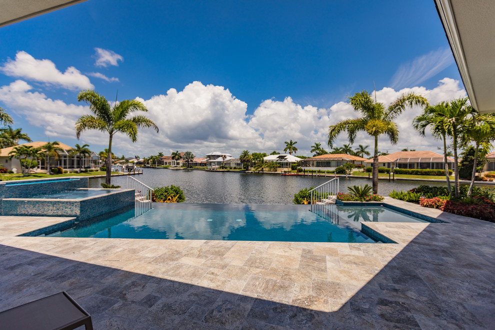 Photo of a mid-sized transitional backyard rectangular infinity pool in Miami with a hot tub and natural stone pavers.