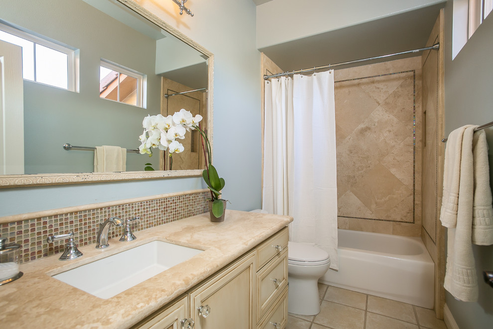 Photo of a small traditional master bathroom in Los Angeles with raised-panel cabinets, beige cabinets, a drop-in tub, a shower/bathtub combo, a one-piece toilet, beige tile, travertine, blue walls, travertine floors, an undermount sink and limestone benchtops.