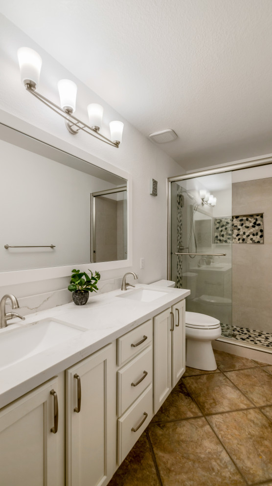 Modern inredning av ett stort vit vitt badrum med dusch, med skåp i shakerstil, vita skåp, en dusch i en alkov, en toalettstol med separat cisternkåpa, grå kakel, porslinskakel, vita väggar, ett undermonterad handfat, bänkskiva i kvarts, dusch med skjutdörr, klinkergolv i porslin och brunt golv