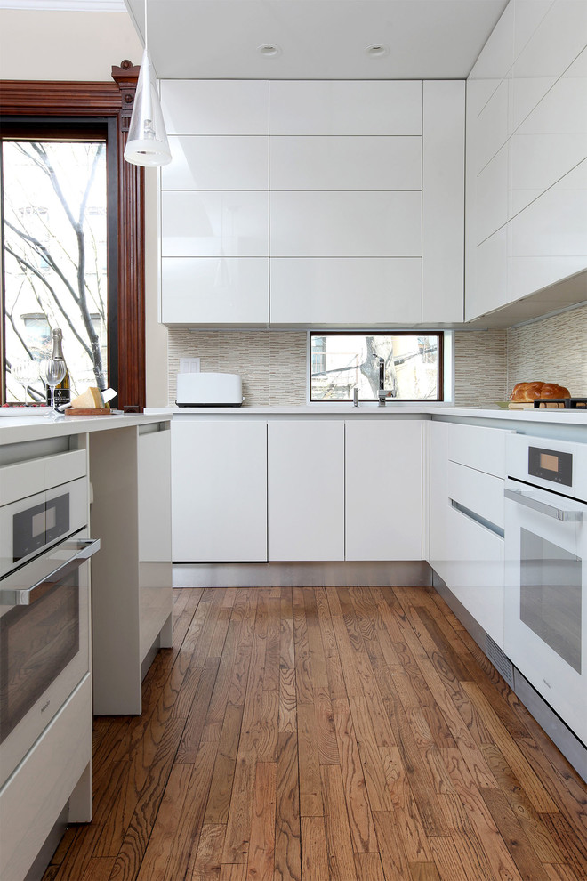 Photo of a mid-sized contemporary l-shaped kitchen in New York with flat-panel cabinets, white cabinets, beige splashback, ceramic splashback, white appliances, dark hardwood floors and a peninsula.