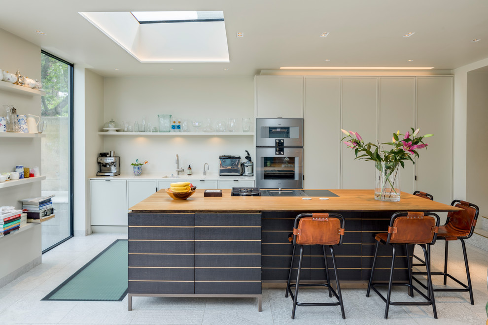 Mid-sized contemporary single-wall open plan kitchen in London with an undermount sink, flat-panel cabinets, white cabinets, quartzite benchtops, stainless steel appliances, cement tiles, with island, grey floor, white benchtop and white splashback.