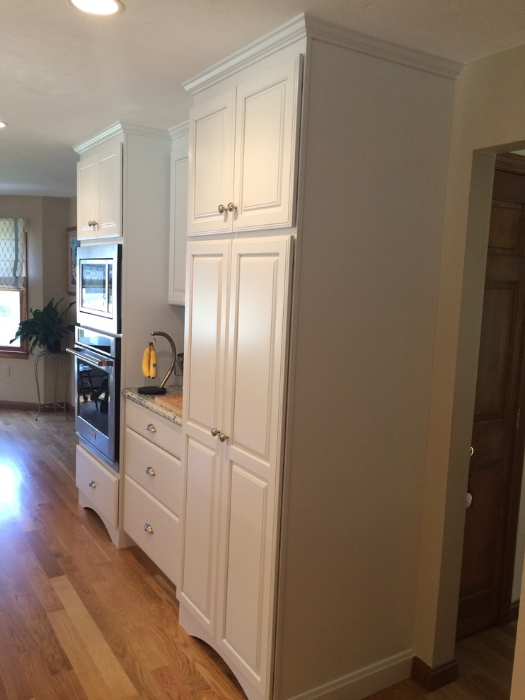 Example of a transitional u-shaped medium tone wood floor eat-in kitchen design in Boston with an undermount sink, raised-panel cabinets, white cabinets, granite countertops, blue backsplash, glass tile backsplash, stainless steel appliances and an island
