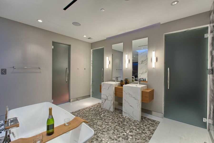 Photo of a large contemporary master wet room bathroom in Los Angeles with open cabinets, medium wood cabinets, a freestanding tub, a two-piece toilet, white tile, stone slab, grey walls, pebble tile floors, an integrated sink, marble benchtops, multi-coloured floor and a hinged shower door.